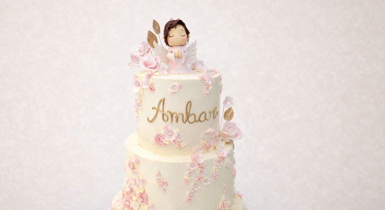 Tarta de comunión con ángel decorativo y flores rosas.
